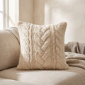 Cream chunky cable knit cushion standing on a linen sofa