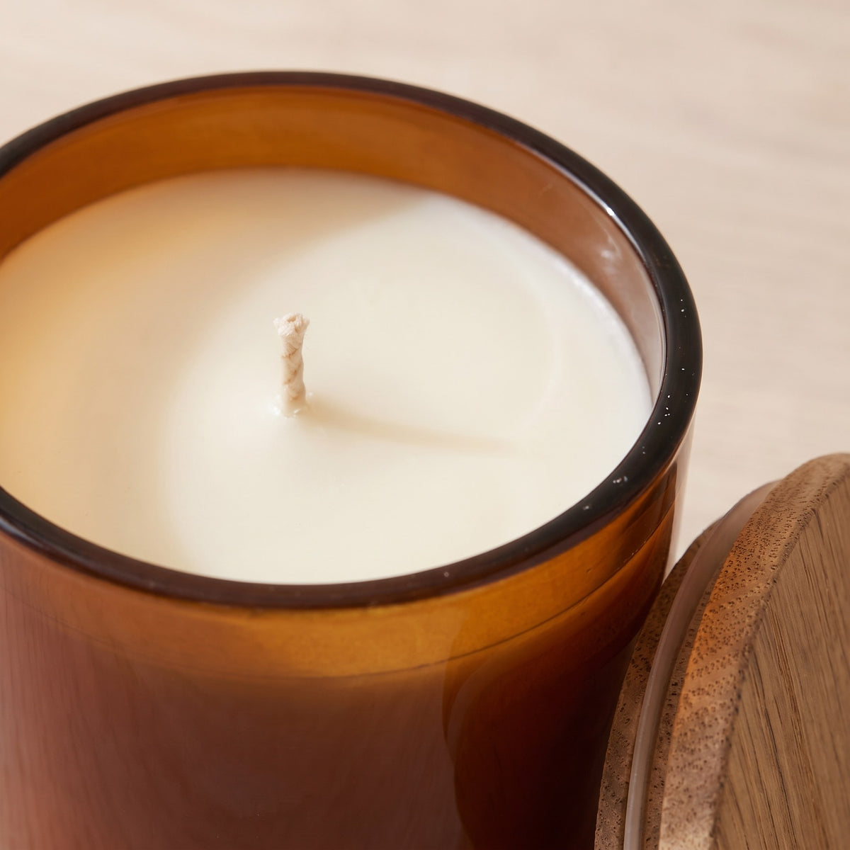 Close-up of the cream wax surface and cotton wick inside the amber glass jar, oak lid beside it
