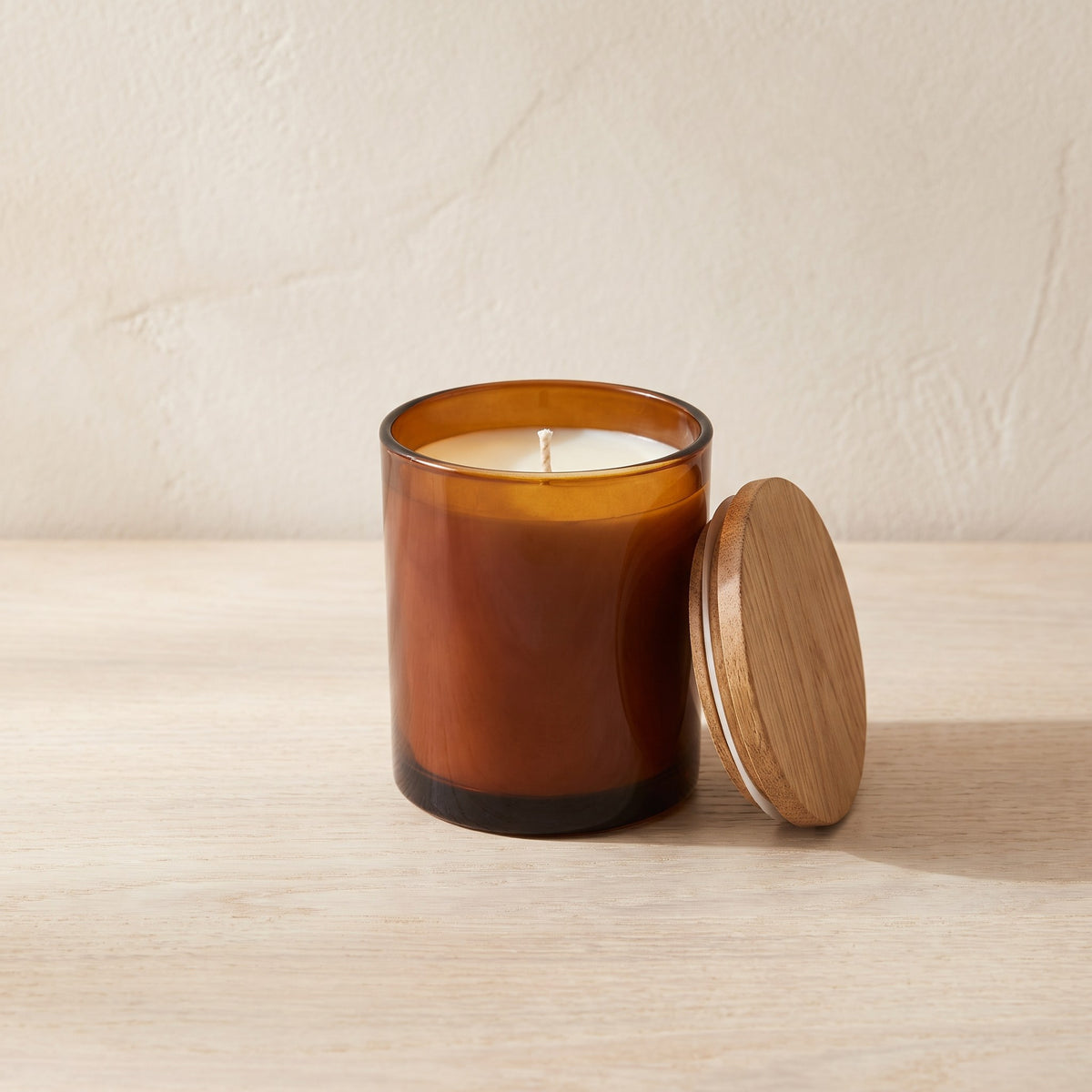 Fig & Cedar Scented Candle in an amber glass jar with its oak lid leaning against it on a pale oak table