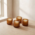 Four ribbed amber glass tealight holders with white tealights on a pale oak table