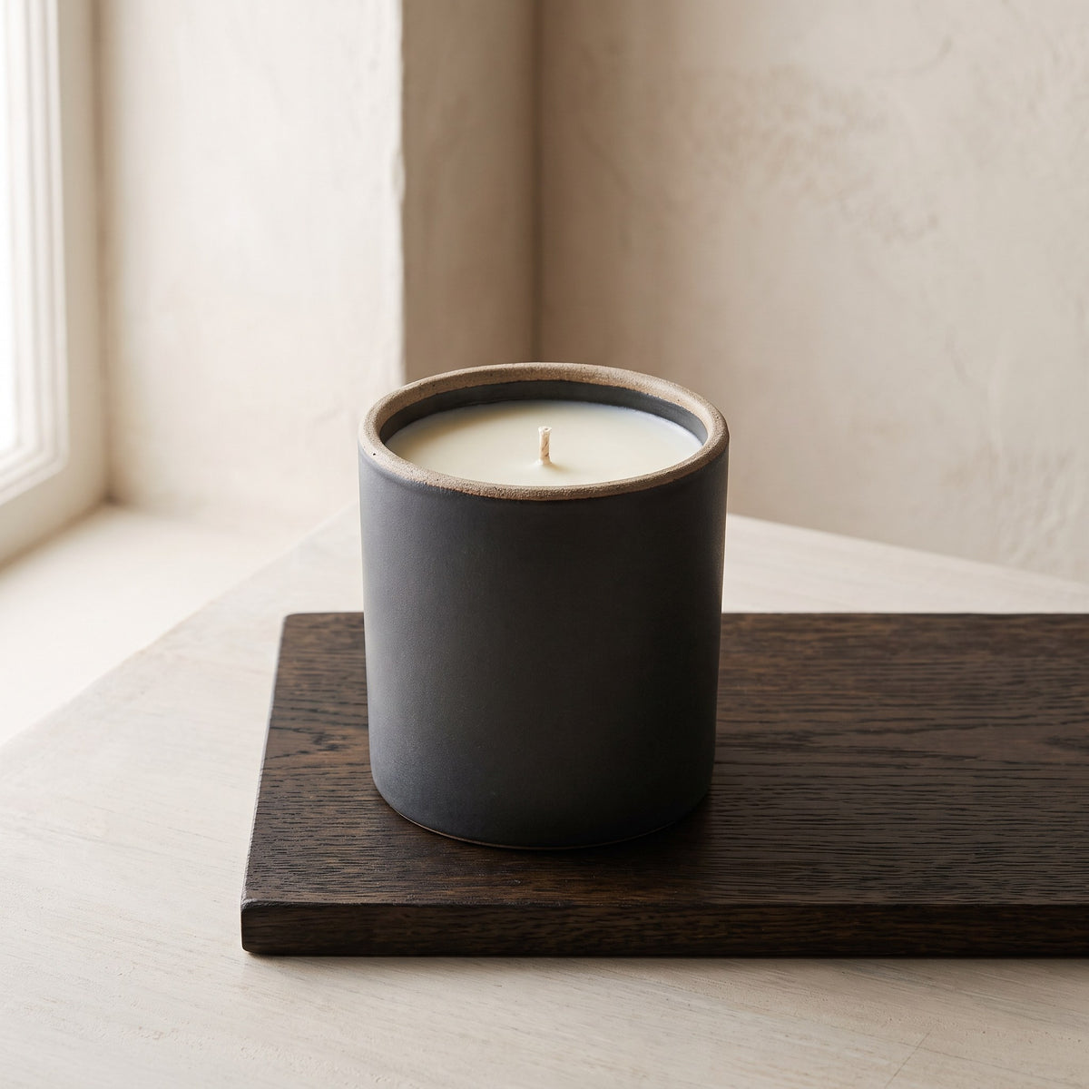 Smoked Oak & Amber candle in a matte charcoal stoneware pot on a dark wooden board