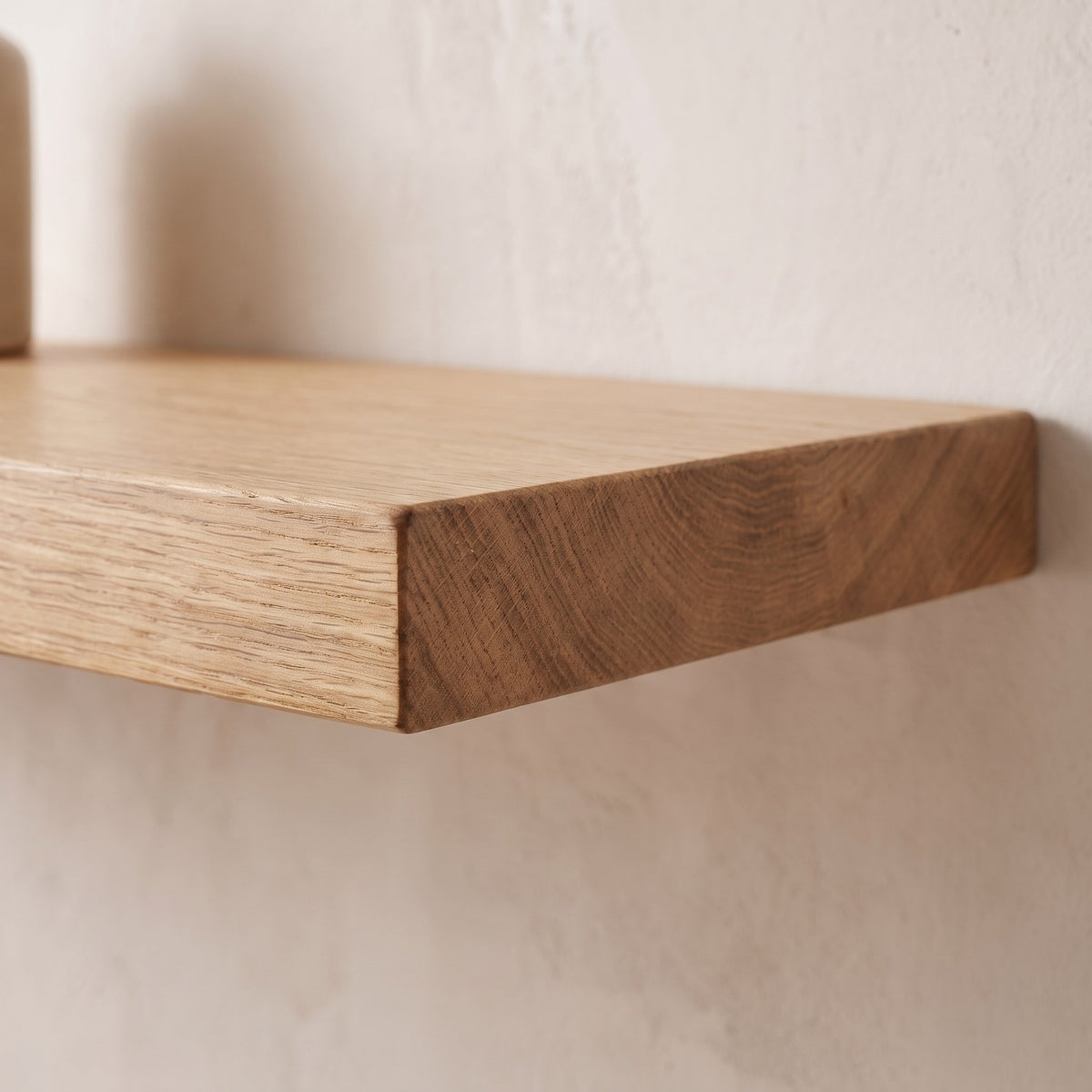 Close-up of the front edge and end grain of the solid oak floating shelf against the wall