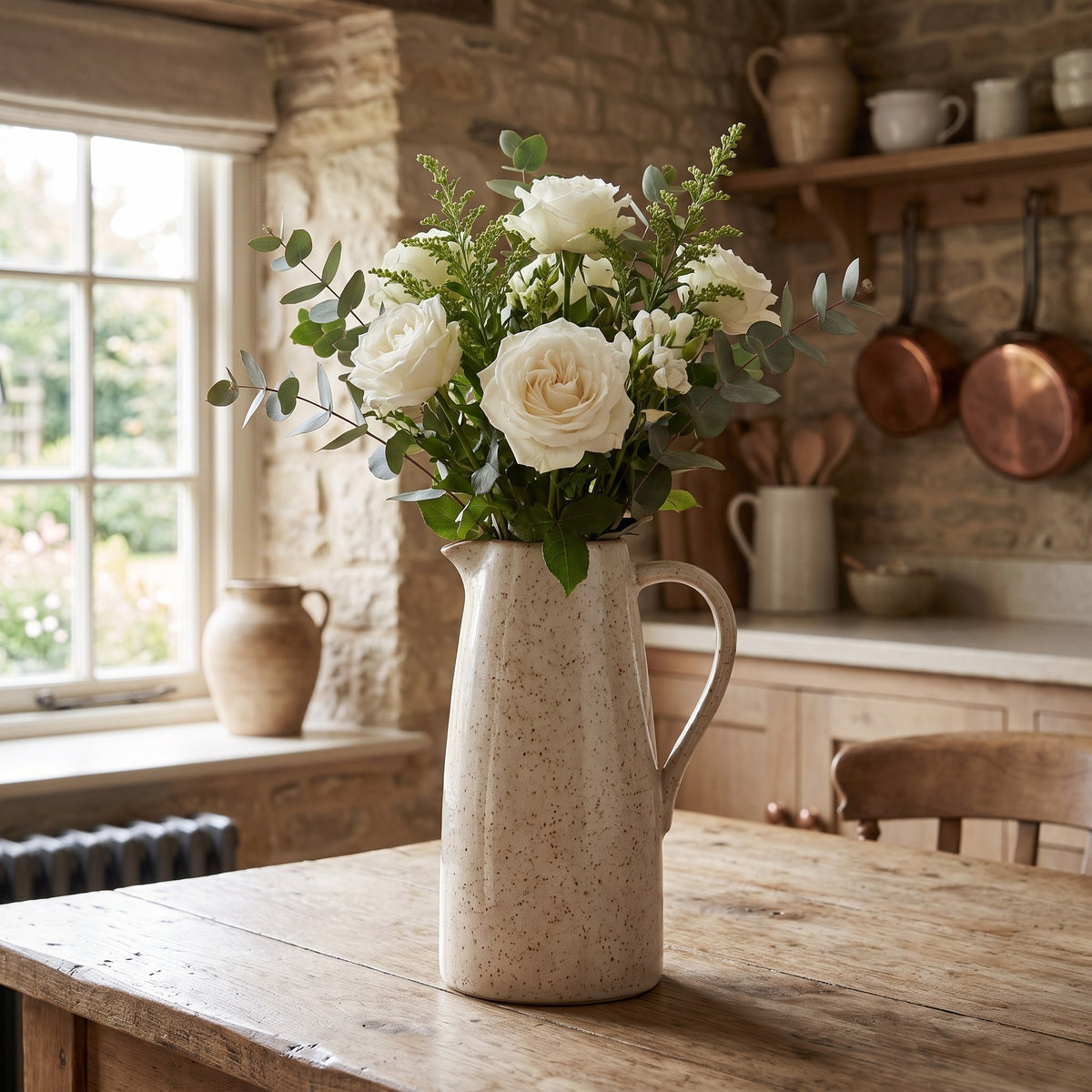Speckled stoneware jug vase with white garden roses on a farmhouse kitchen table