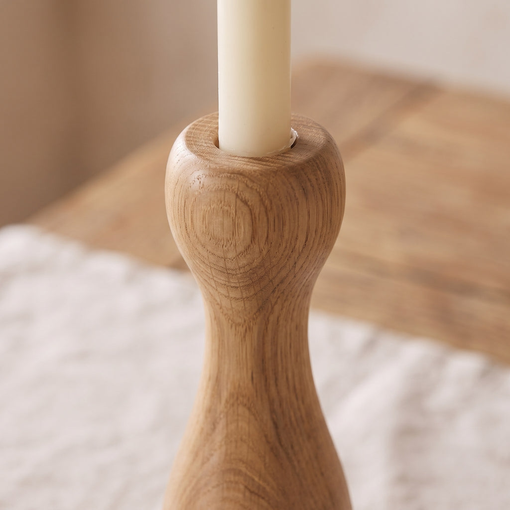 Close-up of the lathe-turned curves and oak grain of one candle holder with the base of a taper candle
