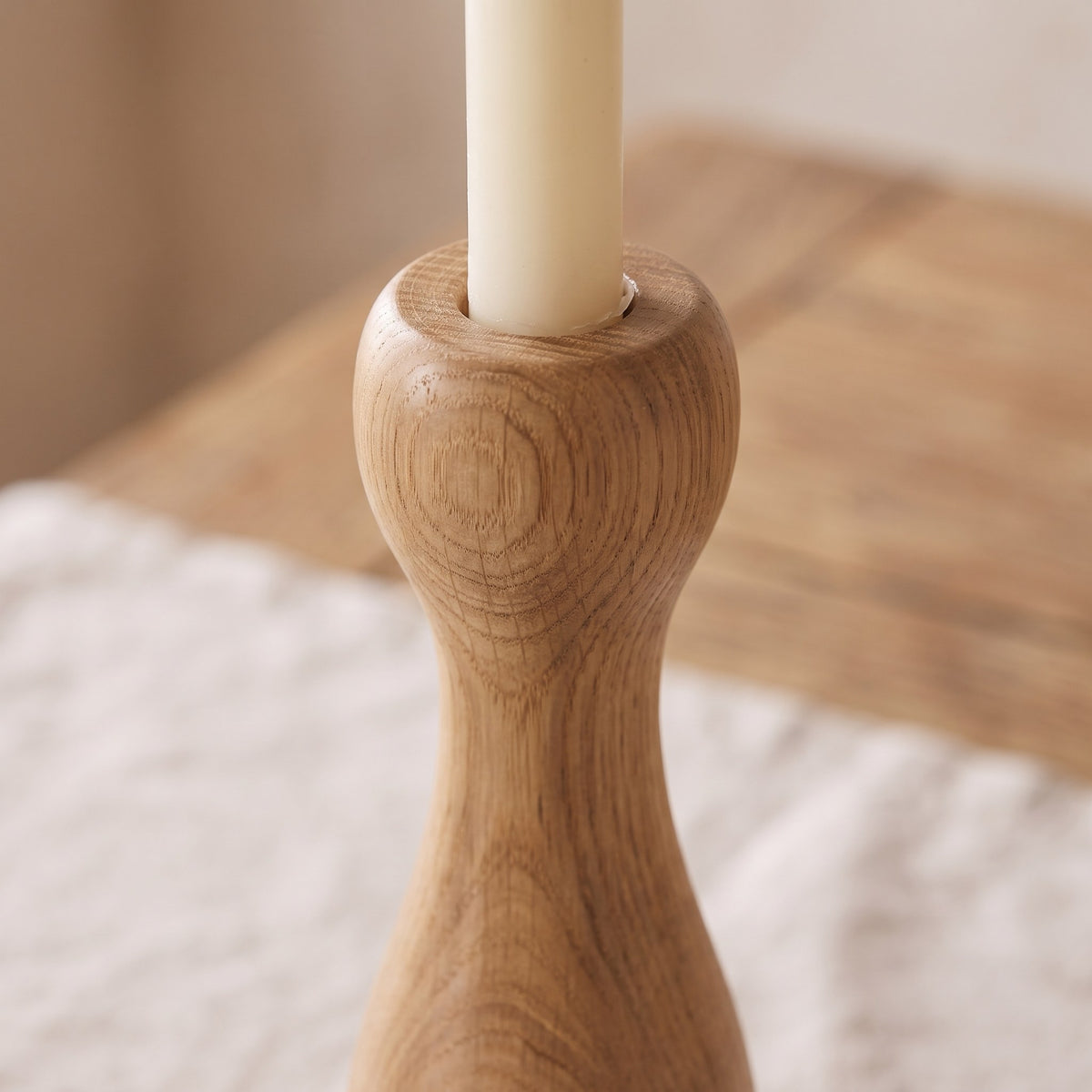 Close-up of the lathe-turned curves and oak grain of one candle holder with the base of a taper candle
