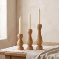 Three turned oak taper candle holders of different heights holding ivory dinner candles on a linen runner