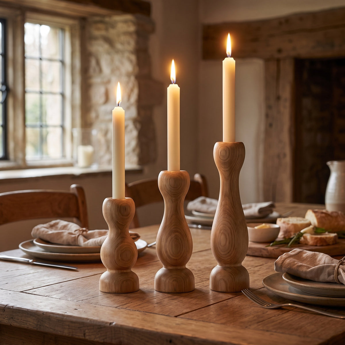 Turned oak candle holders with lit taper candles on a cottage dining table set for supper